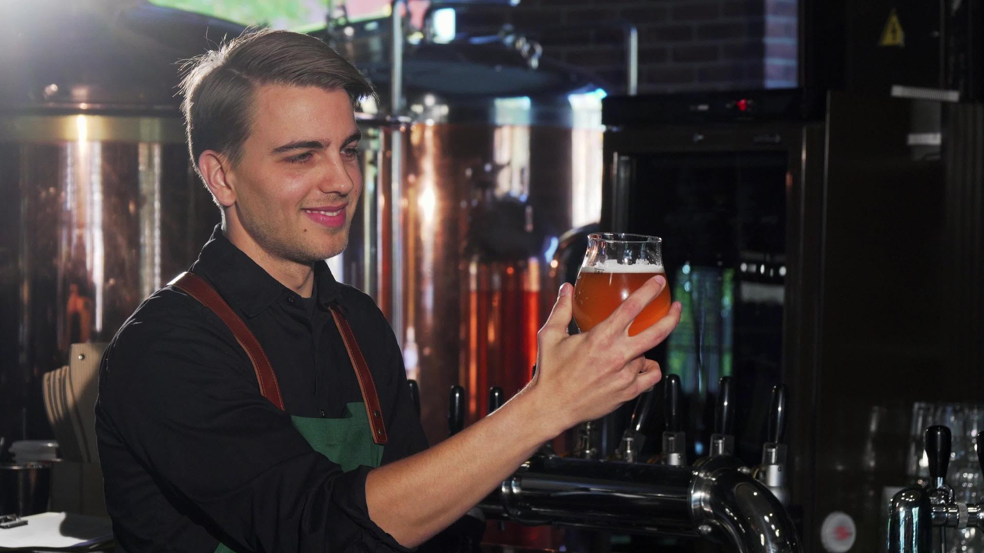 快乐的酒保看着杯子里的啤酒在他的手工艺品啤酒酒吧工作视频的预览图