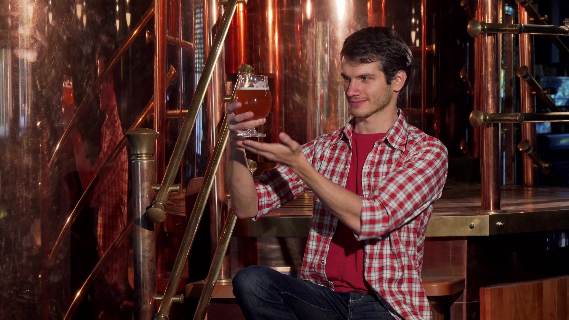 年轻的男性酿酒商在他的酿酒厂检查新鲜酿造的啤酒视频的预览图