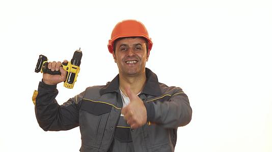 快乐成熟的工业工人戴着硬帽用拇指握着钻头视频的预览图