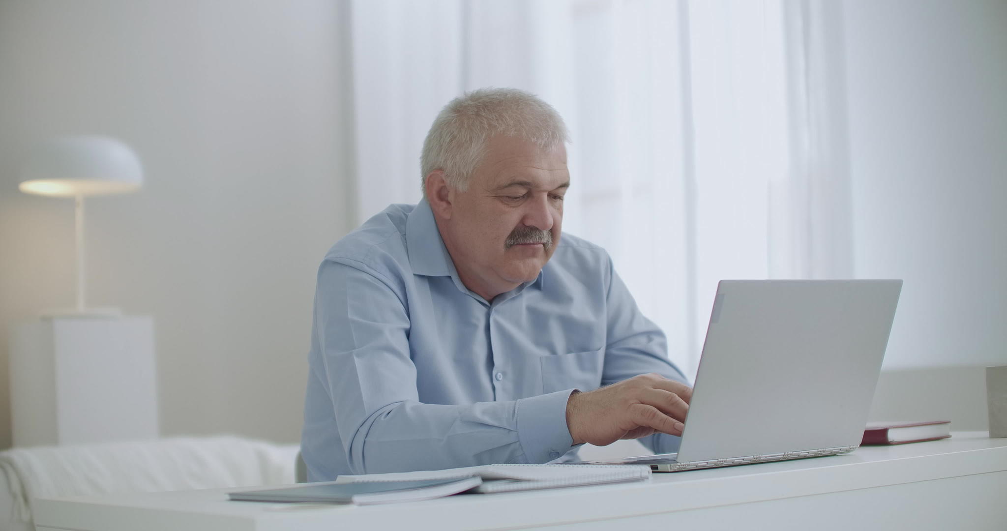 白发男子在家工作在笔记本上打字通过聊天上网上网视频的预览图