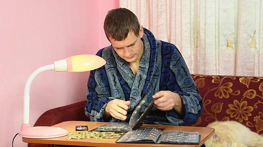 一个穿着睡衣的年轻人看着他在专辑中收集的硬币视频的预览图