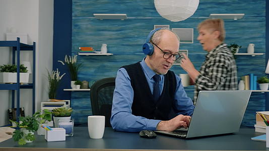 老年人在笔记本电脑工作时使用耳机听音乐视频的预览图