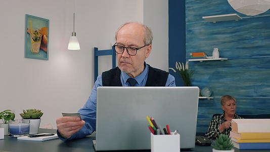 退休男子在网上购物用信用卡在笔记本电脑上付款视频的预览图