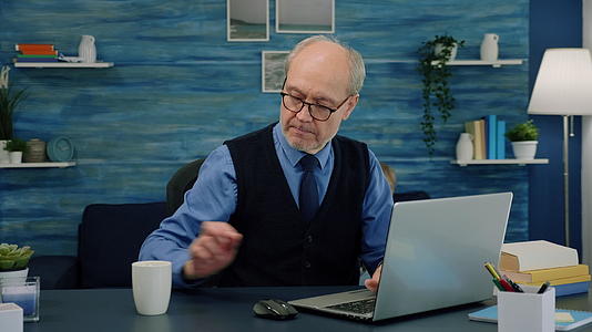 老人坐在桌旁喝咖啡看书用笔记本电脑打字视频的预览图