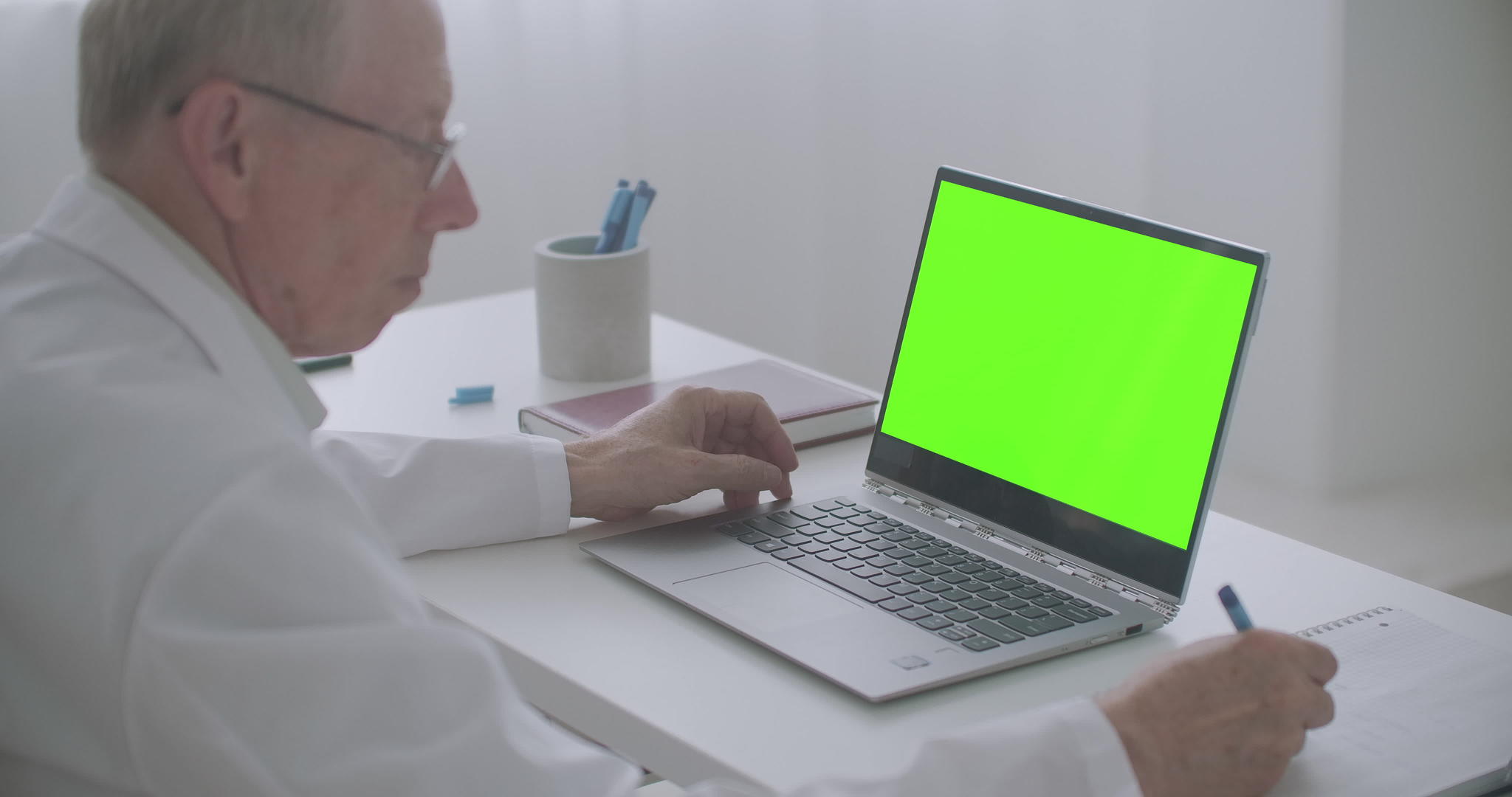 老年男性医生正在网上阅读文章查看笔记本电脑和写作视频的预览图