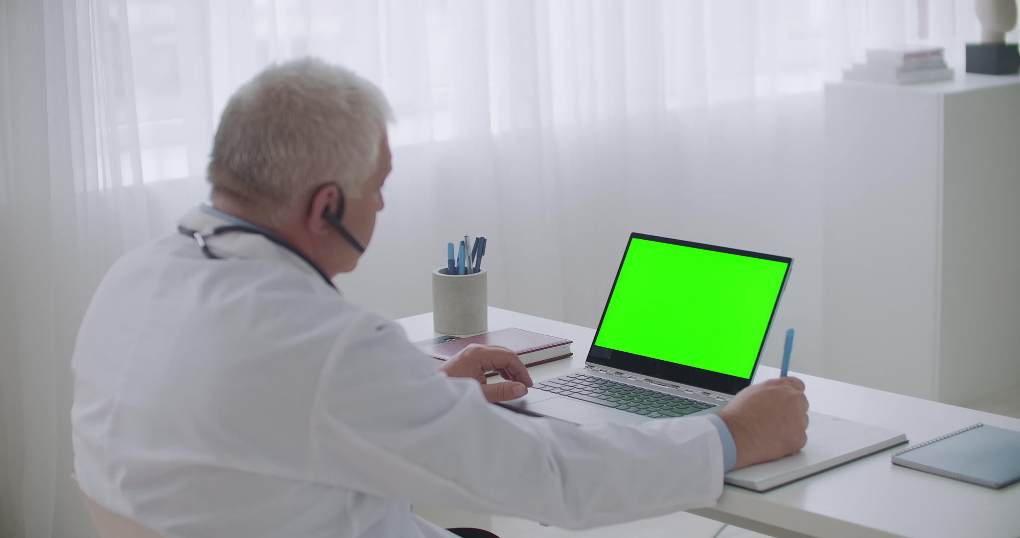 老年男医生正在听在线研讨会或患者在笔记本电脑上使用视频的预览图