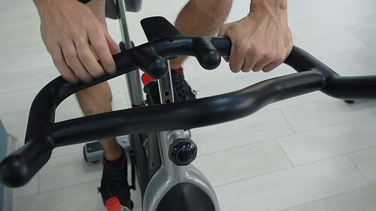 男性手在健身俱乐部握着手柄静态自行车运动员在健身房视频的预览图