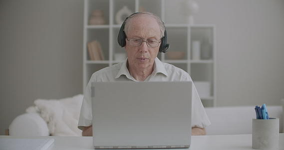 老年男性教授通过家庭视频电话笔记本电脑和耳机进行交流视频的预览图