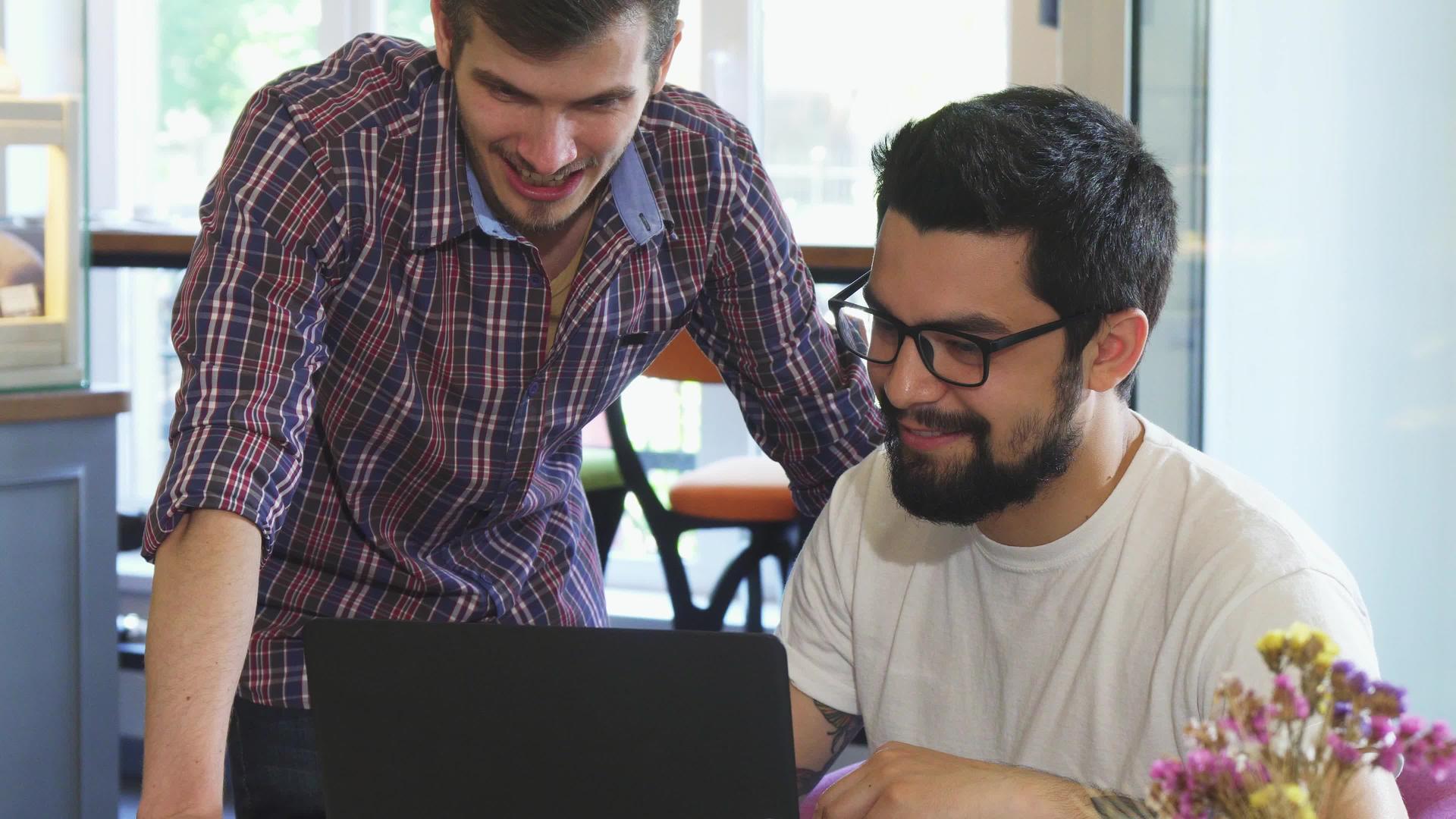 两个年轻人在咖啡店一起用笔记本电脑视频的预览图