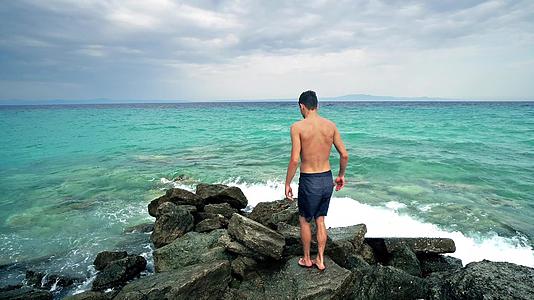 孤独的男孩站在海岩和航海地平线上视频的预览图