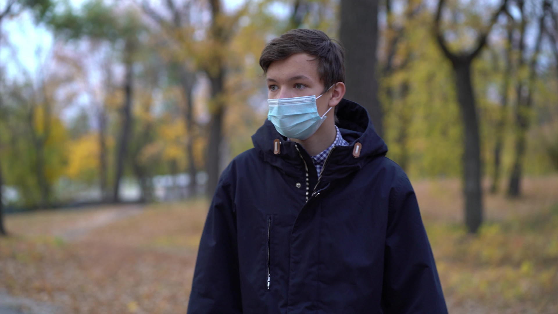 戴着医用面具的男孩在公园里走来走去视频的预览图