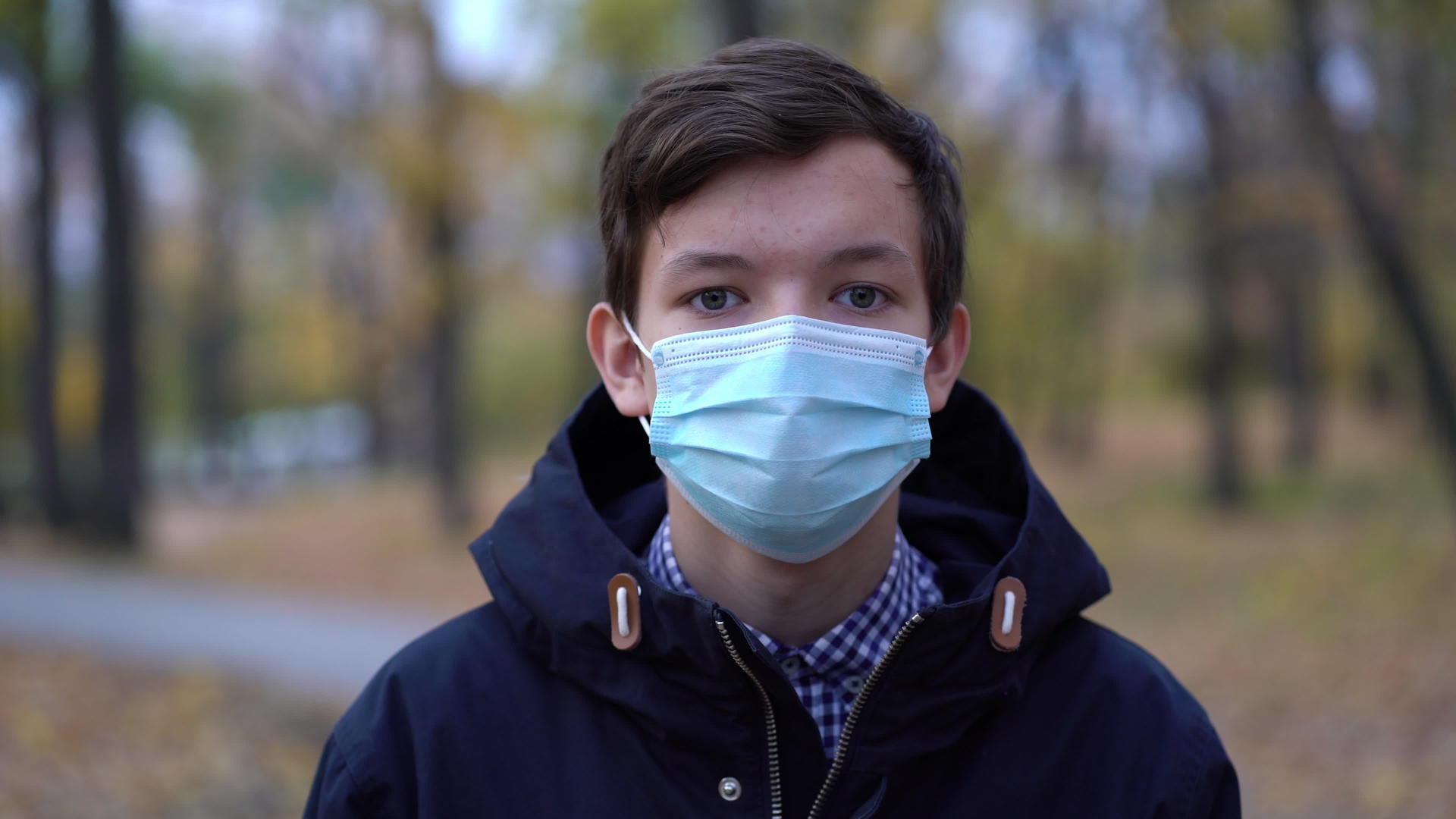 戴着医用面具的男孩在公园里走来走去视频的预览图