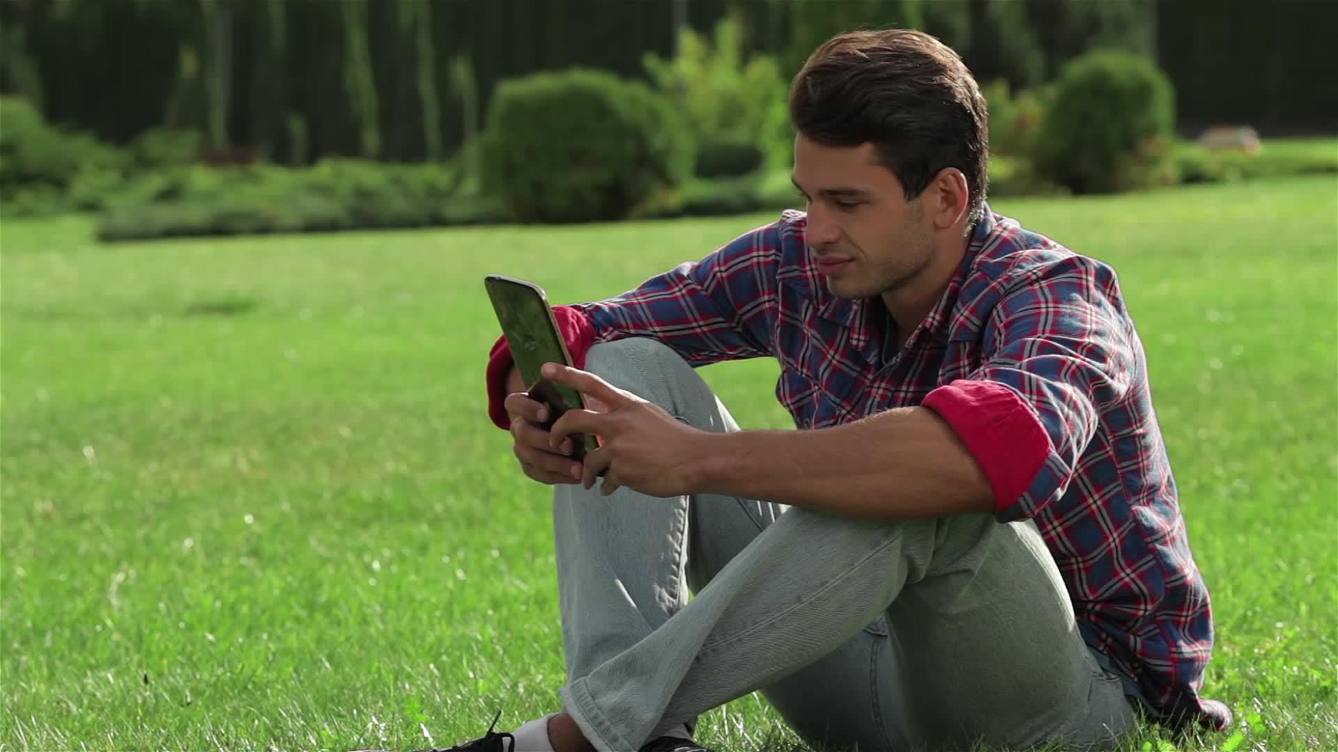 男人坐在草地上使用平板电脑视频的预览图