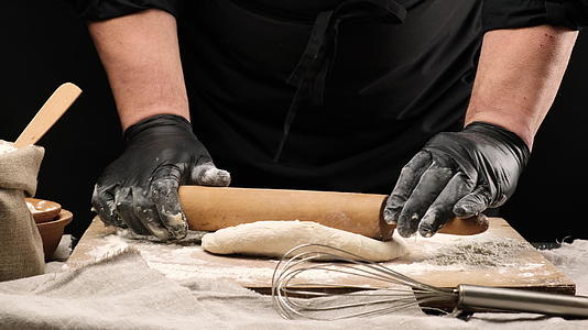 两个男人戴着黑色乳胶手套用木头从白面粉上慢慢滚动针头视频的预览图