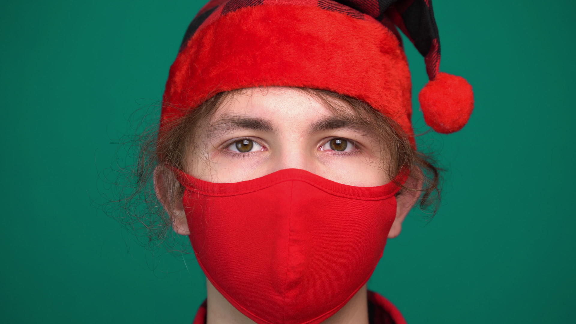 戴着红色医疗面具的圣塔帽男孩的肖像看着相机视频的预览图