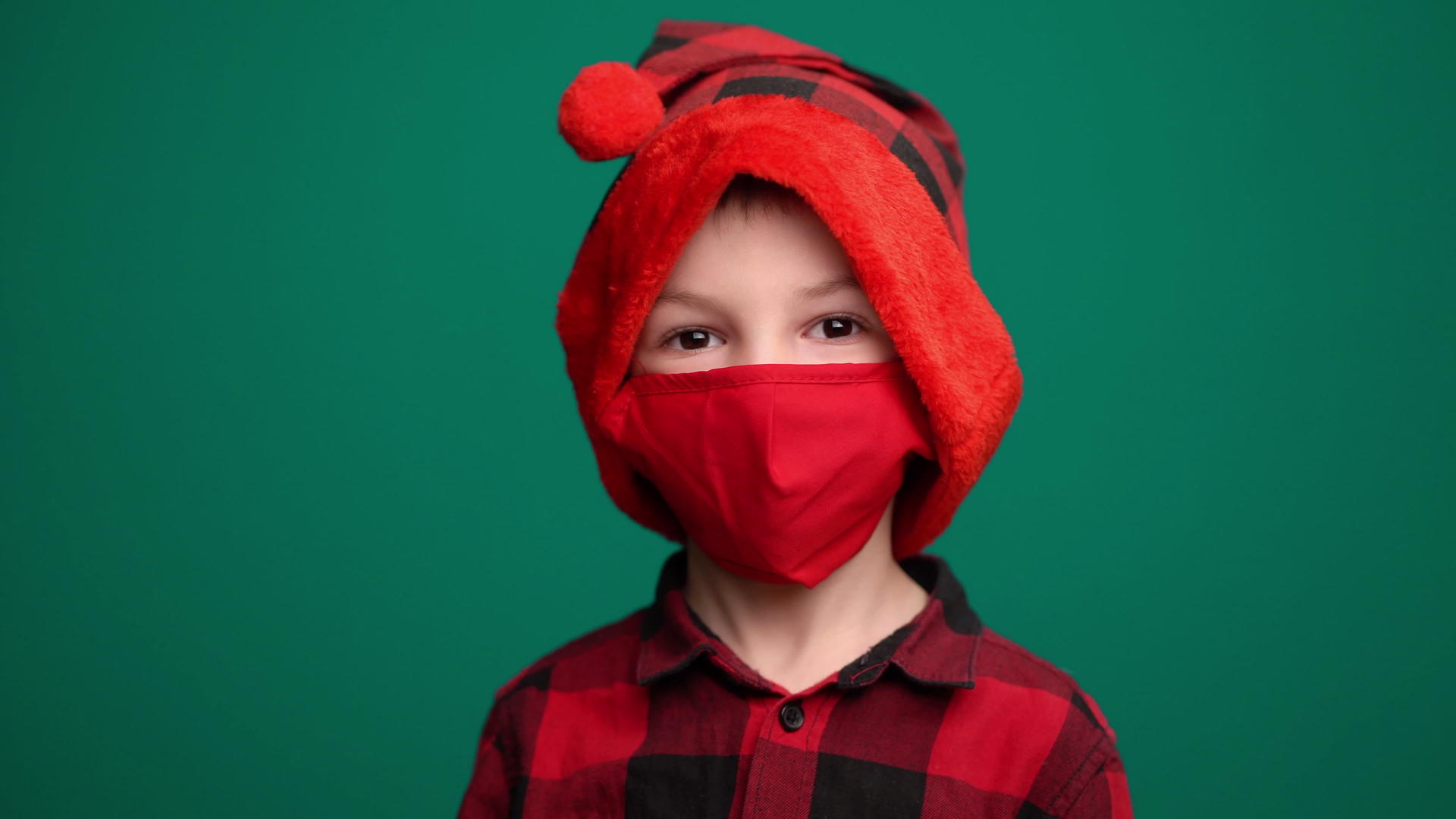 小男孩戴着红色医疗面具戴着圣塔帽看着相机视频的预览图