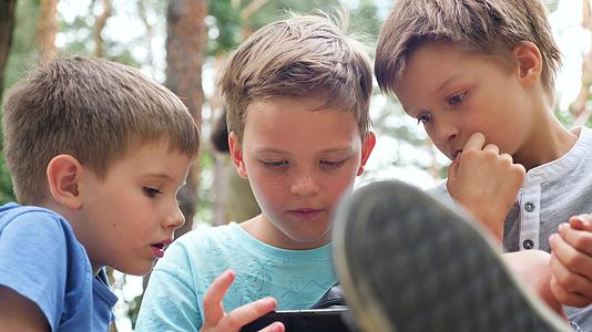 脸上有雀斑的男孩看着手机孩子们兄弟姐妹看着手机三个男孩视频的预览图