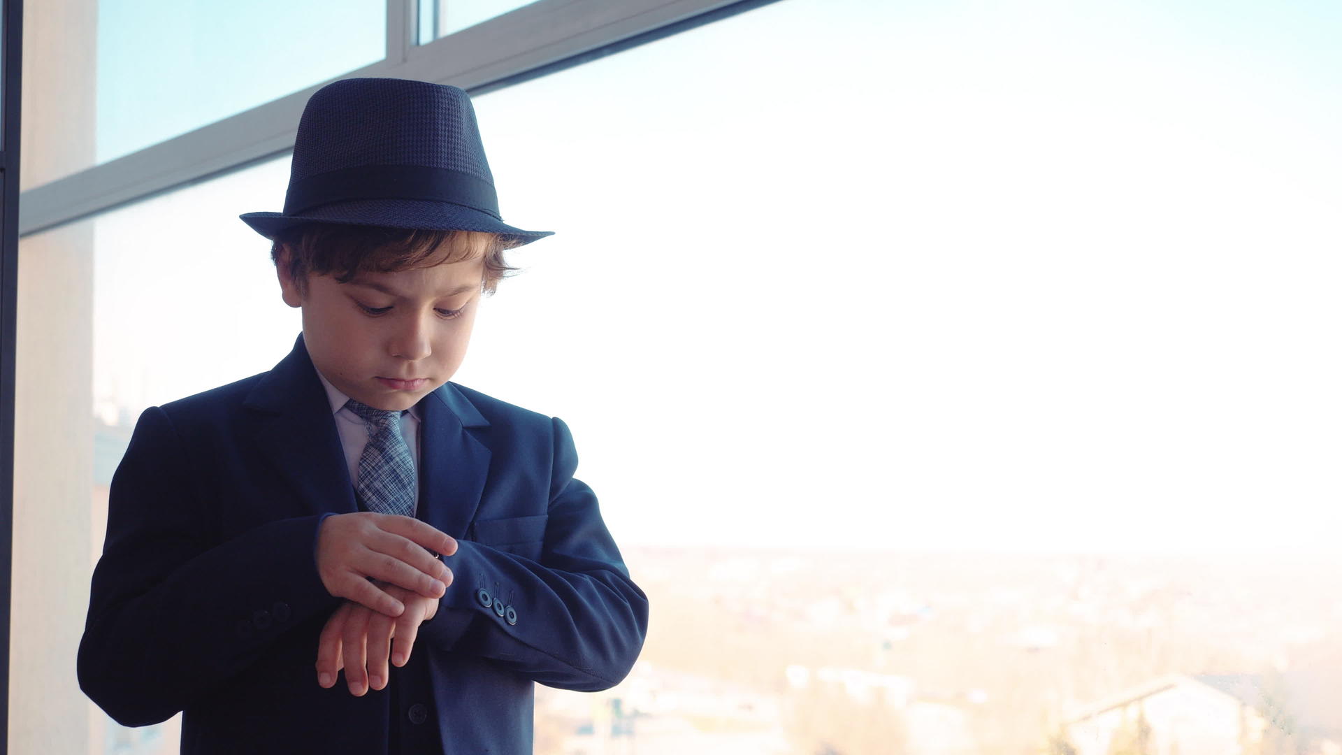 办公室里穿着西装和帽子的小男孩的商人正在看窗户然后看着手表视频的预览图