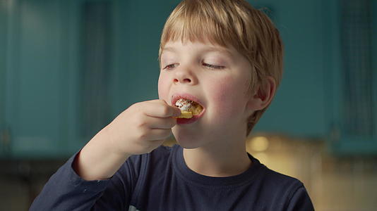 金发学龄前男孩喜欢吃奶油华夫饼站在蓝色厨房里视频的预览图