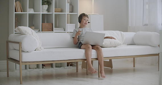 小男孩坐在家里的沙发上通过笔记本和朋友通过视频电话视频的预览图