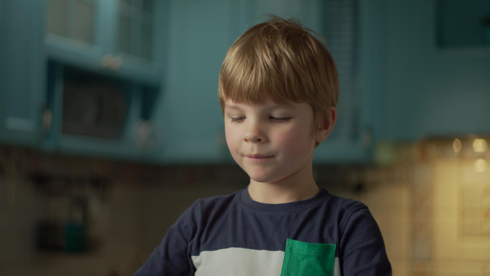 金发学龄前男孩喜欢吃巧克力棒站在蓝色厨房里视频的预览图