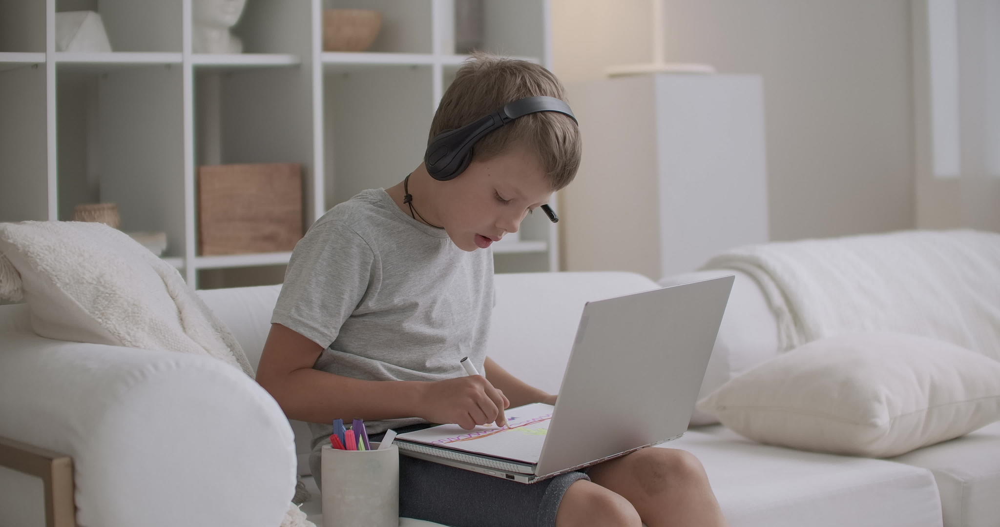学龄前男孩正在学习在家画画他们通过笔记本电脑、电脑、耳机进行监控视频的预览图