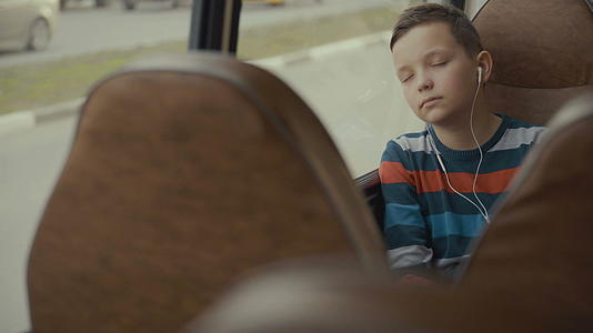 一个男孩乘公共汽车穿过城市近距离拍摄他听音乐视频的预览图