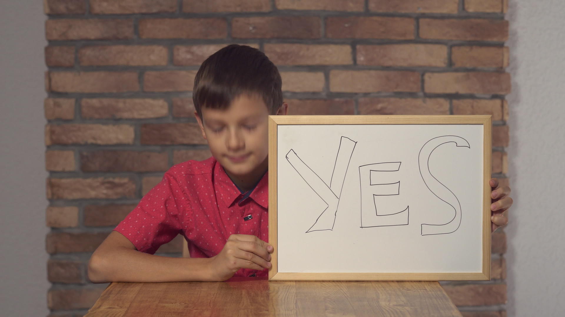 坐在桌子上的孩子拿着翻页的字母YEA背景红砖墙视频的预览图