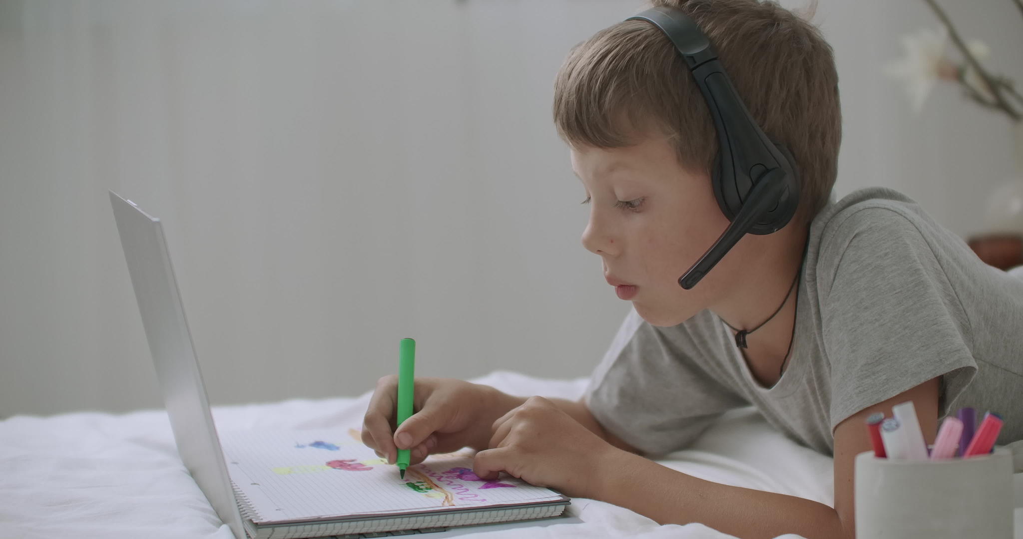 看着笔记本电脑屏幕和书画的小男孩肖像用耳机监视视频的预览图