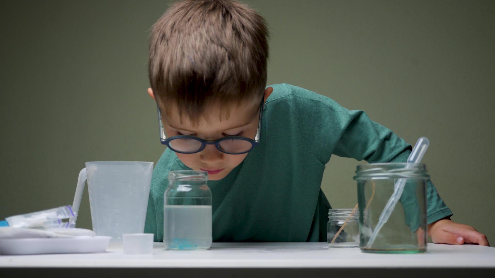 戴眼镜的男孩在室内用吸管和液体进行化学实验视频的预览图