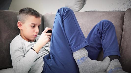 男孩坐在沙发上用智能手机玩电子游戏视频的预览图