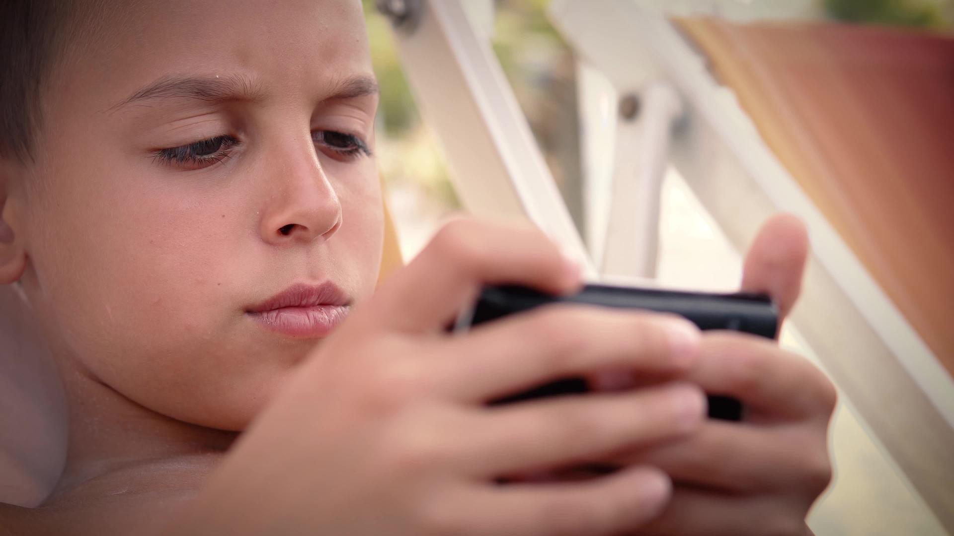 暑假期间男孩躺在沙滩床上在智能手机上玩游戏视频的预览图