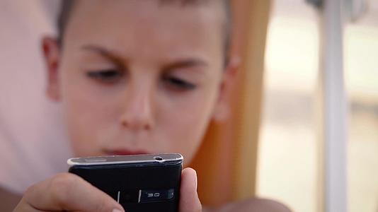 暑假期间男孩坐在阴影下玩智能手机游戏视频的预览图
