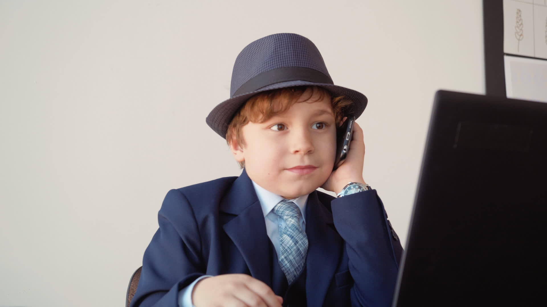 小男孩在商务办公室用手机前的笔记本电脑打电话视频的预览图