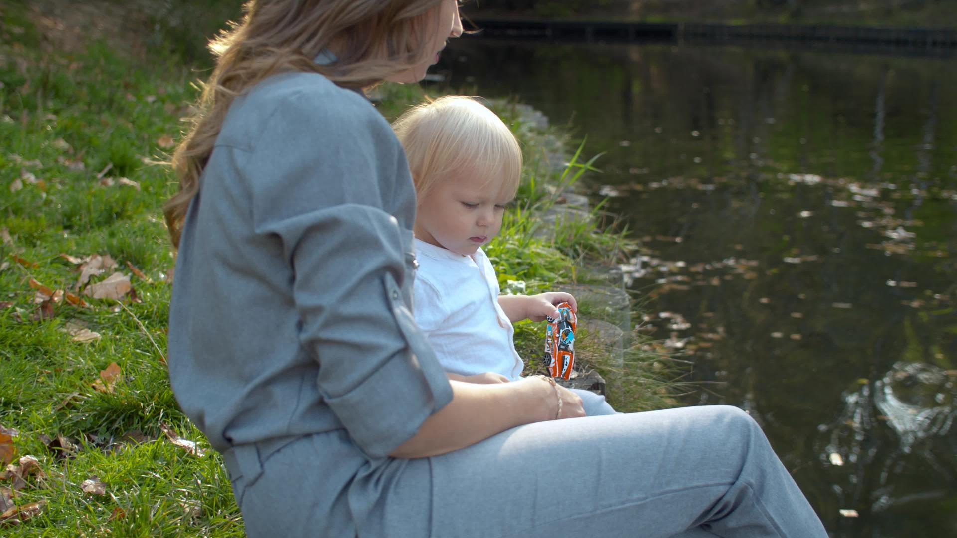 一位年轻的母亲和她的孩子坐在湖边视频的预览图