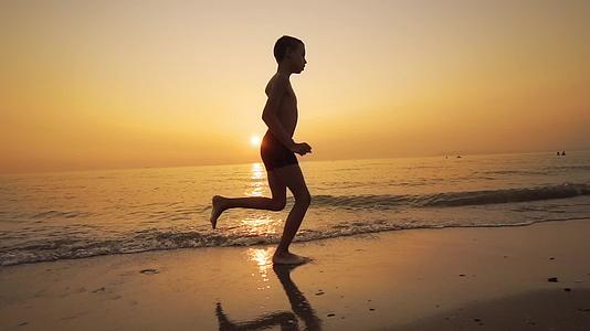 一个孩子在海滩上慢跑被一个橙色的日落和水线慢跑视频的预览图