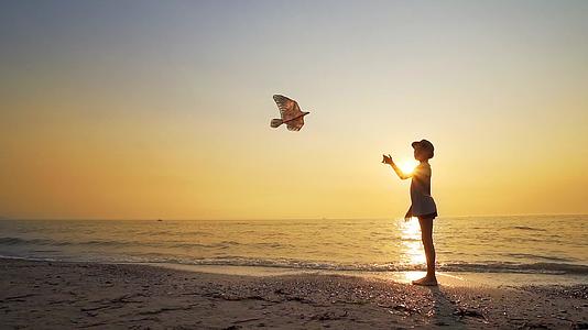在海滩上玩风筝的年轻男孩和夕阳下慢慢移动的日落视频的预览图