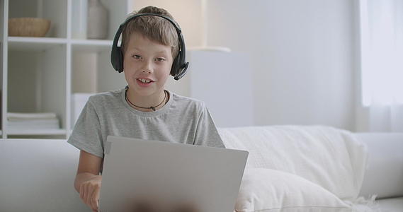 小男孩正在使用带有网络摄像头和无线耳机的现代笔记本电脑视频的预览图