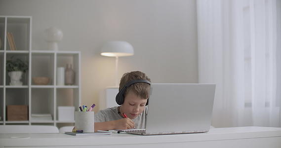 学校男生听童话通过笔记本电脑和绘画耳机独自坐在房间的桌子上视频的预览图