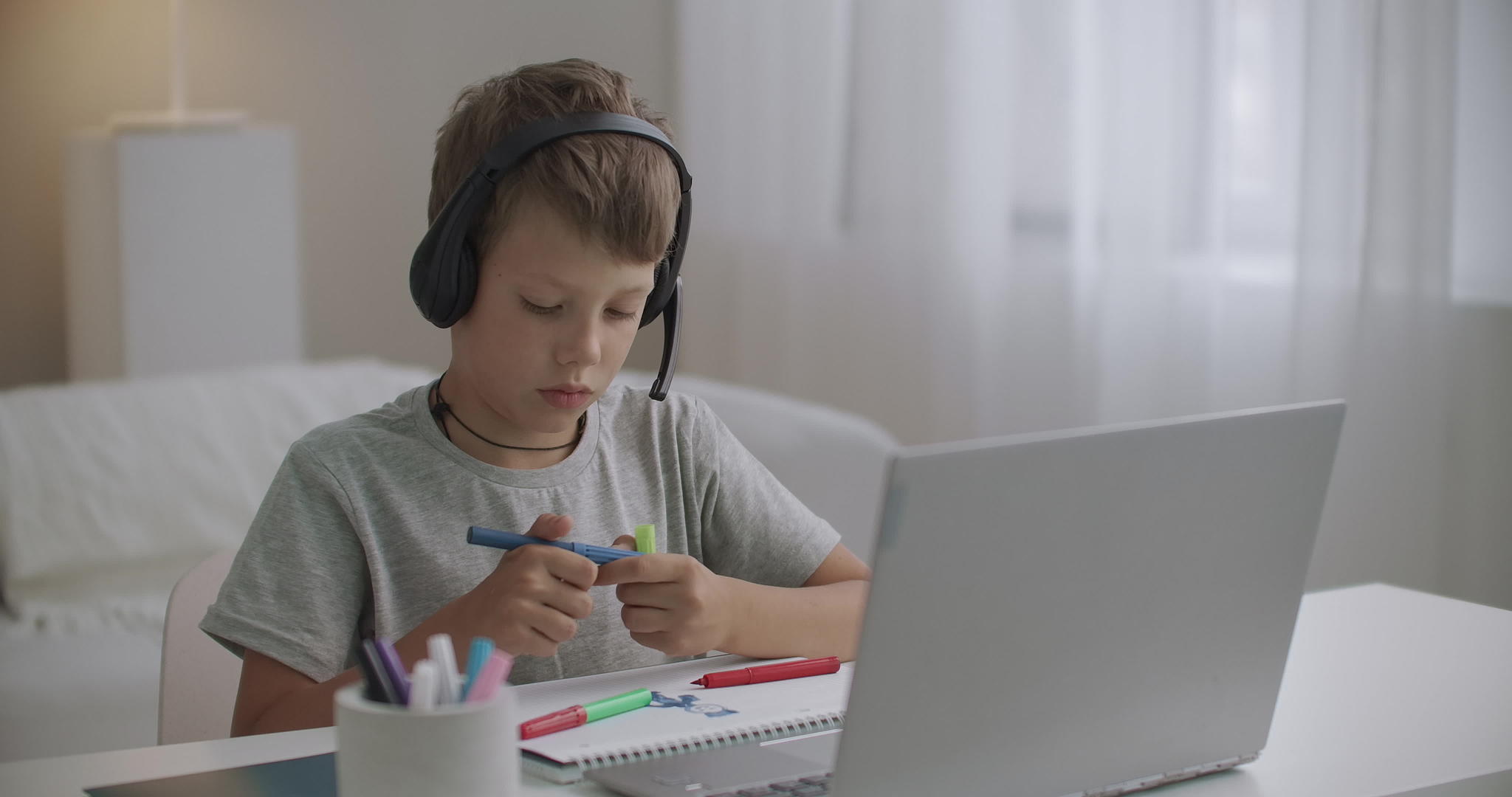 小男孩在家里用笔记本电脑、耳机和彩色铅笔画画视频的预览图