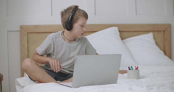 学龄前男孩在网上与朋友或父母一起使用笔记本电脑和耳机视频的预览图