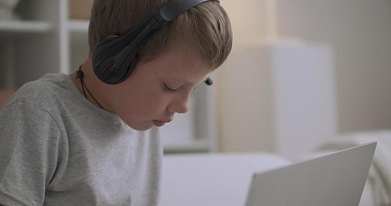 小男孩在家里戴着耳机孩子们在书上画画听音乐视频的预览图