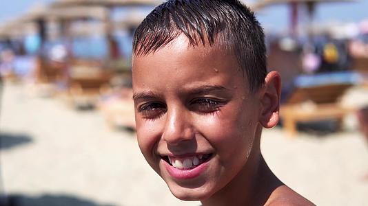 海滩上英俊的男孩看着镜头微笑着孩子们在夏天的阳光下闪耀视频的预览图