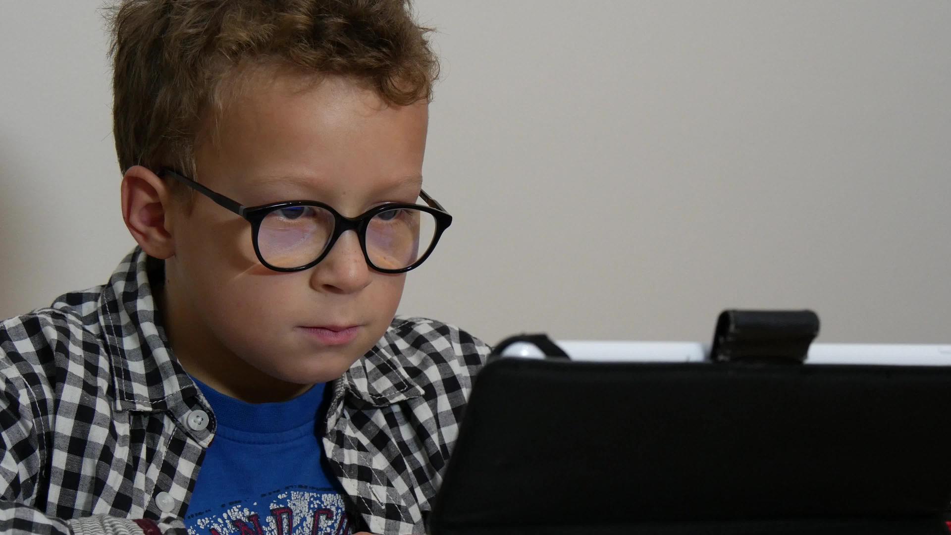 一个带着平板电脑的男孩坐在家里的桌子上视频的预览图