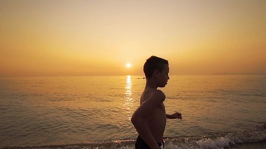 日落时男孩在热带海滩上慢跑视频的预览图