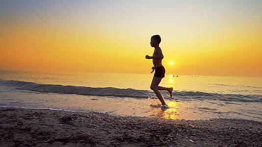 男孩跑来跑去在海滩上慢跑以避免日落以避免日落视频的预览图