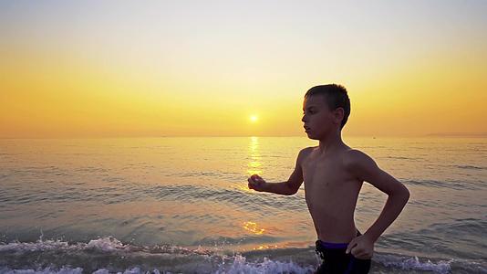 男孩跑来跑去在海滩上慢跑以避免日落以避免日落视频的预览图