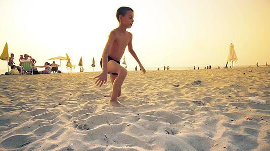 小男孩在海滩上跑日落时翻身视频的预览图