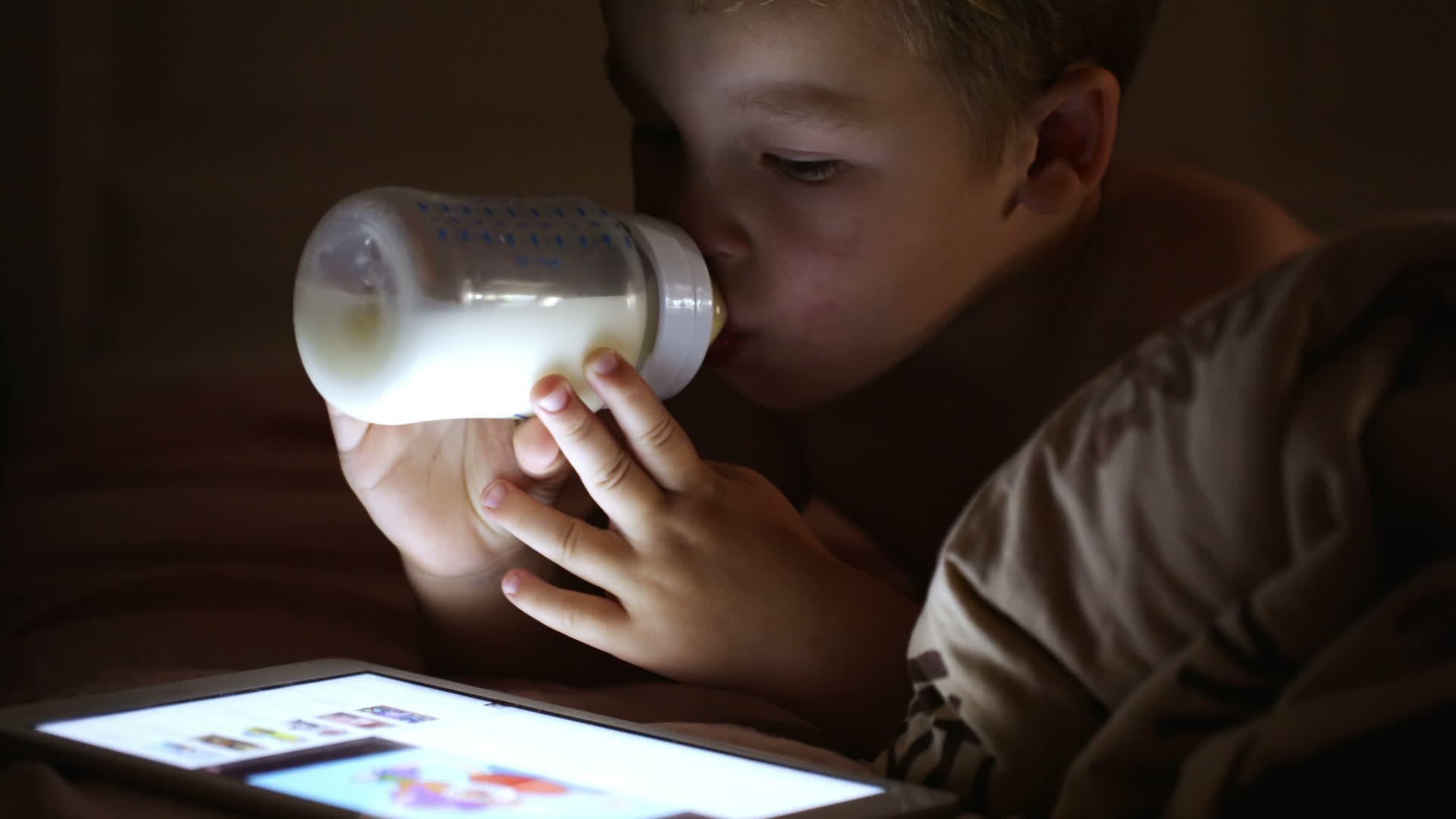 男孩喝着瓶子里的牛奶看着触摸板视频的预览图