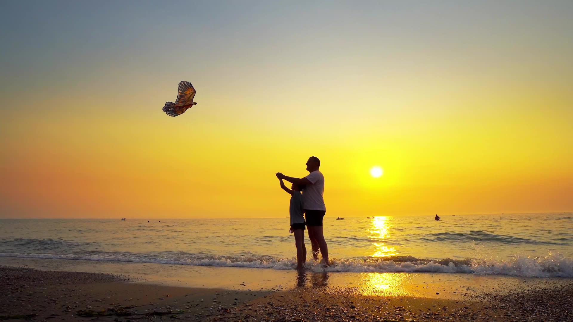 父亲和儿子在海边放风筝橙色的日落视频的预览图